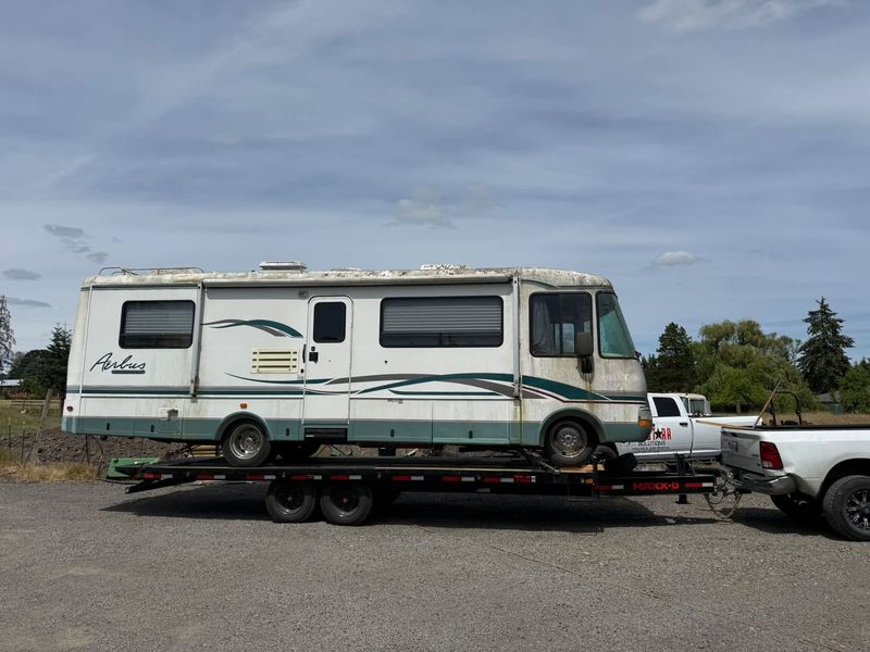Class A motorhome loaded on a flatbed trailer behind the AllStarr Solutions truck