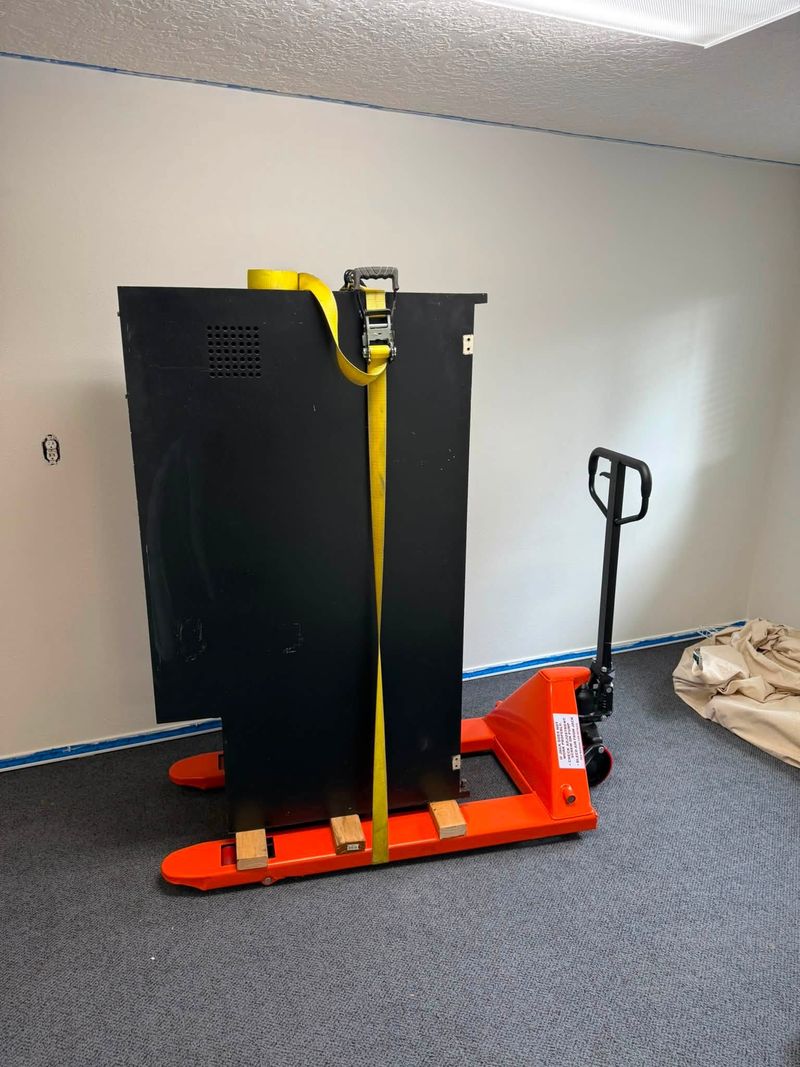 Heavy steel cabinet strapped upright to a pallet jack for removal from an office