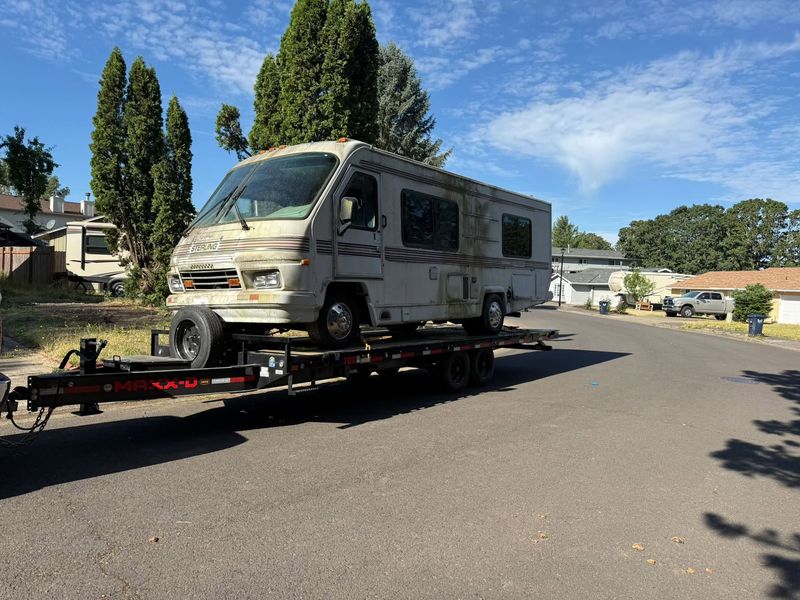 Weathered Sterling motorhome loaded on a flatbed trailer in a residential street