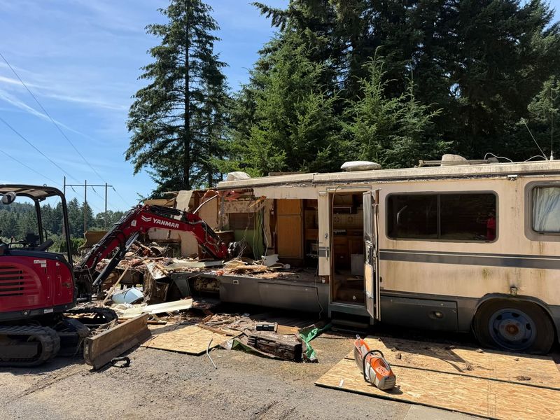 Mini excavator tearing down a motorhome on site, showing why RVs have to be demolished before disposal