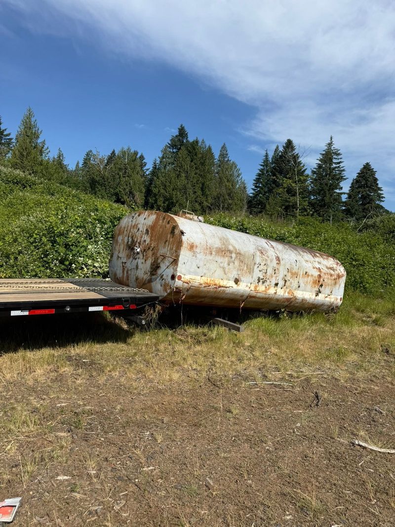 Large rusted steel tank on the ground beside a flatbed trailer before loading