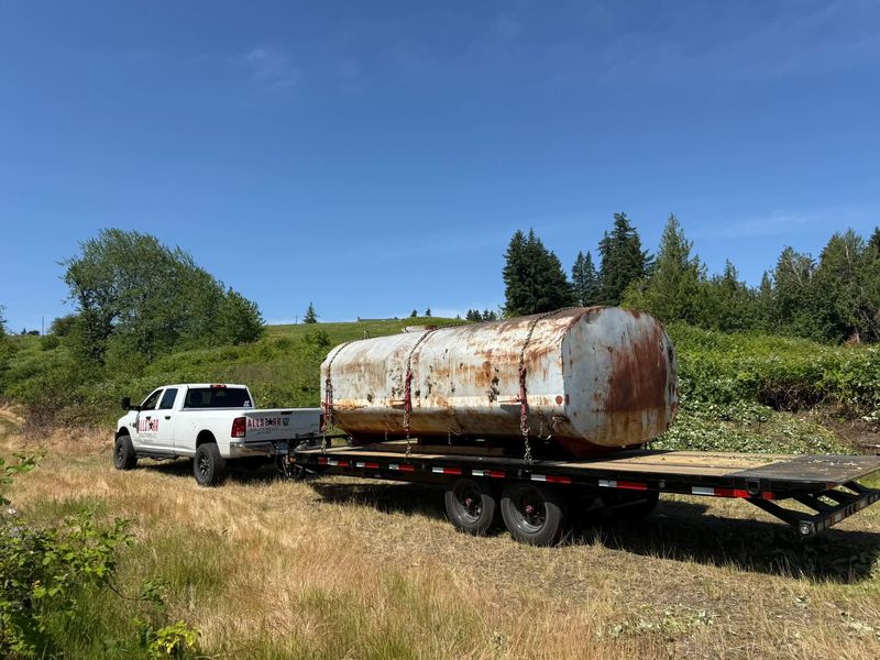 AllStarr Solutions truck hauling a large rusted steel tank chained to a flatbed trailer