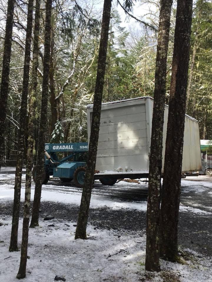 Telehandler lifting a box trailer through snowy woods during a heavy haul