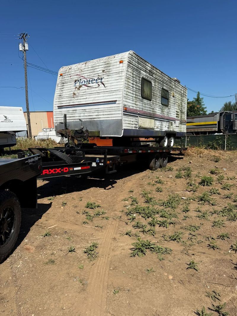Weathered Pioneer travel trailer loaded on a flatbed trailer for disposal