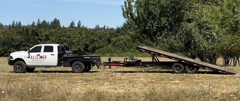 AllStarr Solutions pickup towing a MAXX-D tilt-deck flatbed trailer with the ramp lowered, parked in an Oregon field