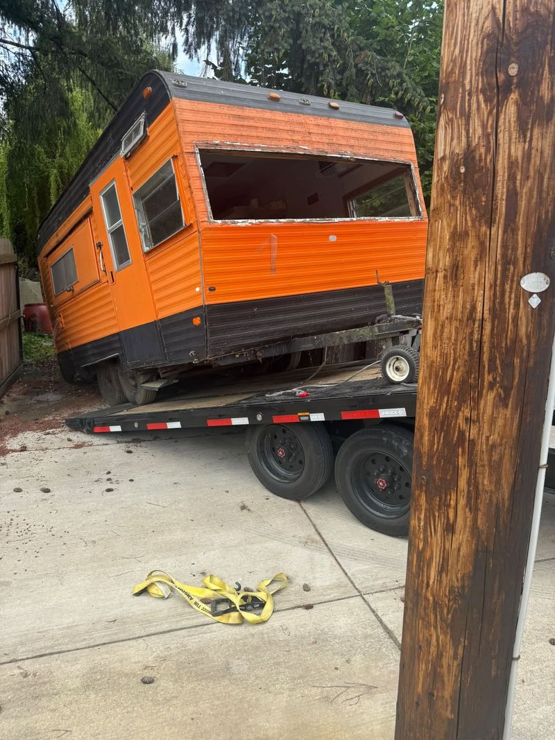 Vintage orange camper trailer being winched up onto a flatbed trailer in a driveway